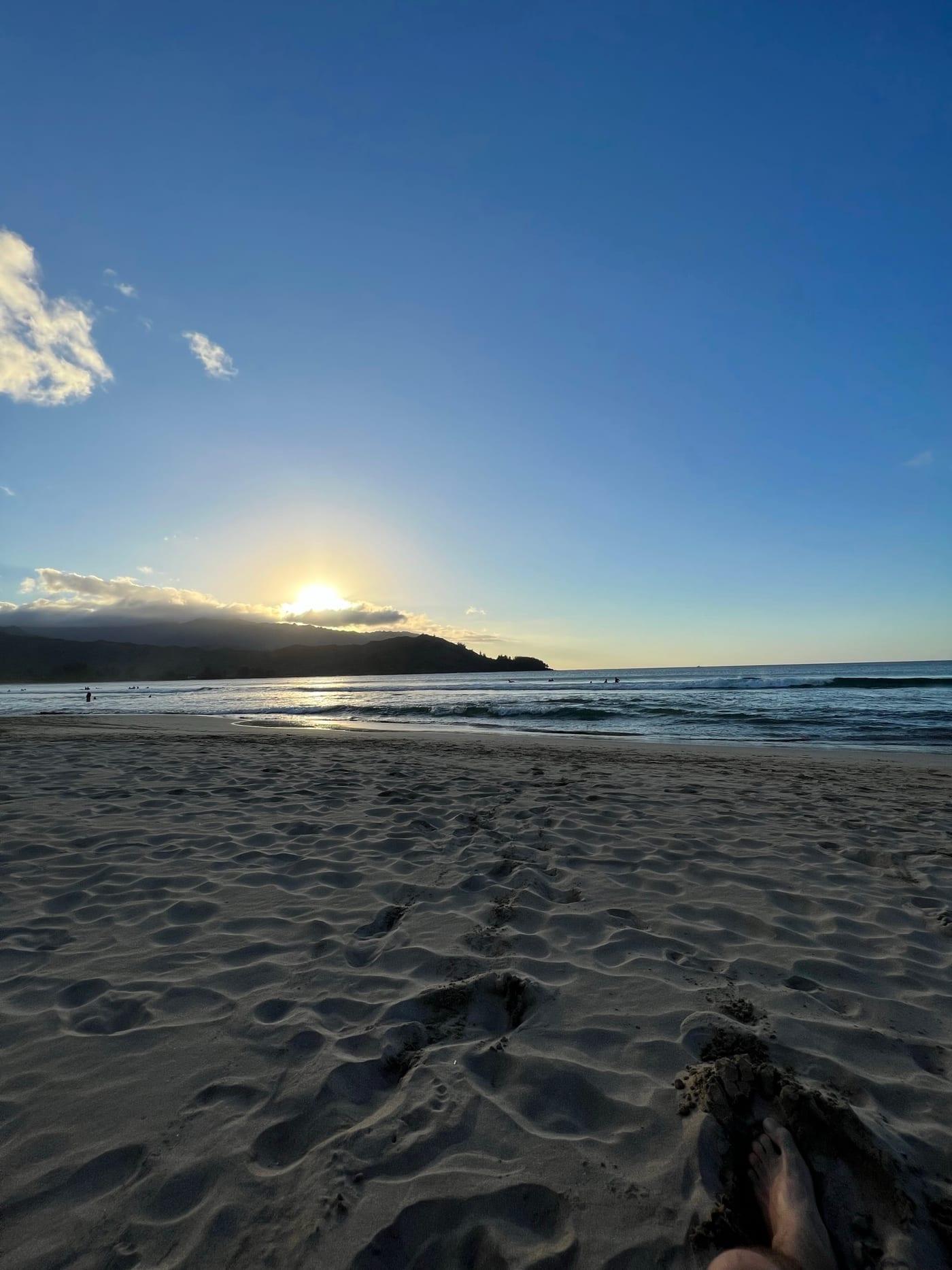 Footprints and feet in the sand at Hanalei Bay at sunset on Kauai's North Shore