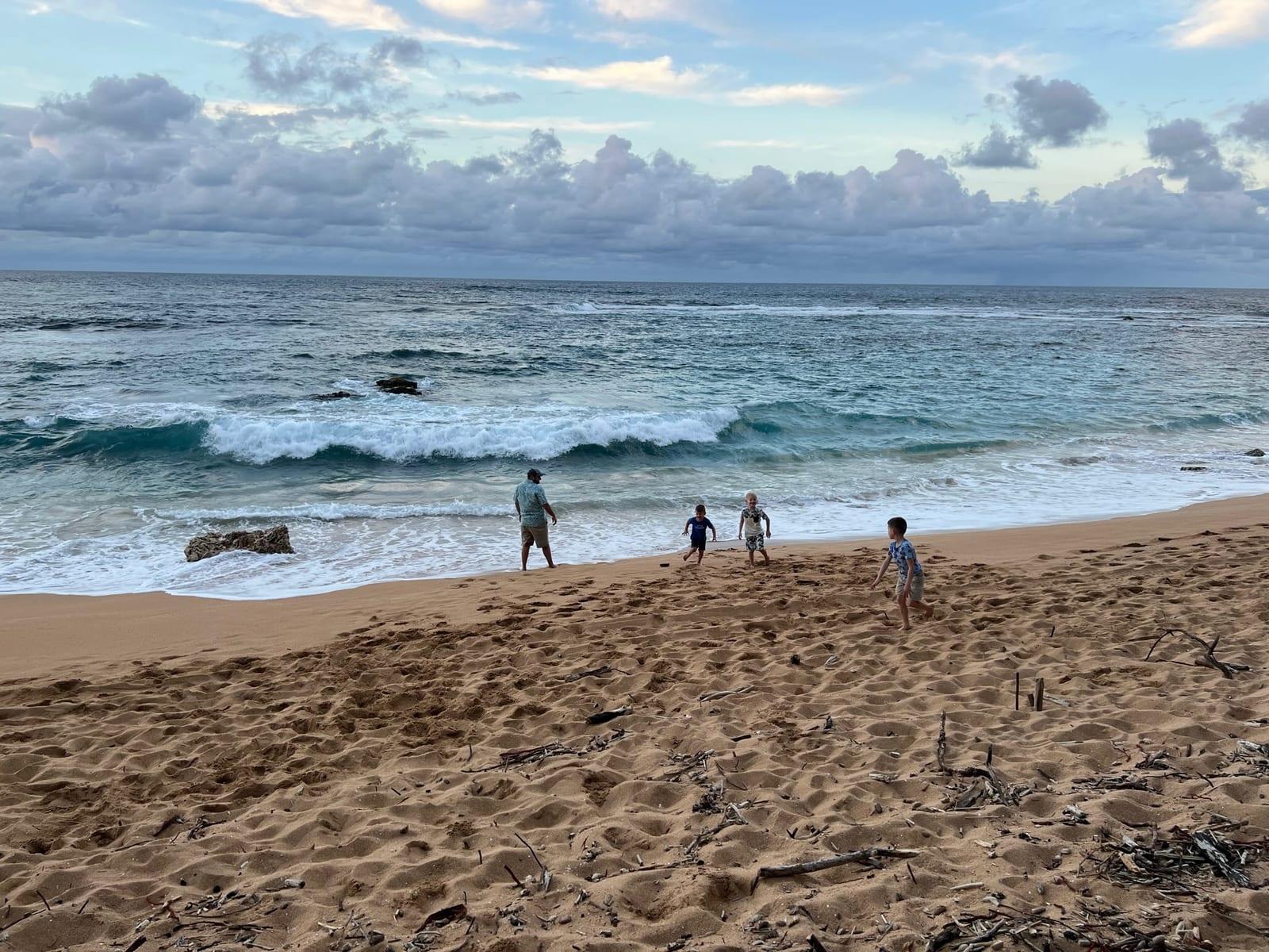 Kids and a parent on the sand at the Tunnels Beach area on Kauai's North Shore at golden hour
