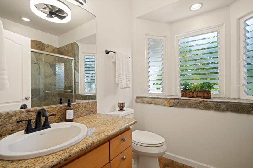 Half bath with stone-tile shower and plantation shutters at Emmalani Hale