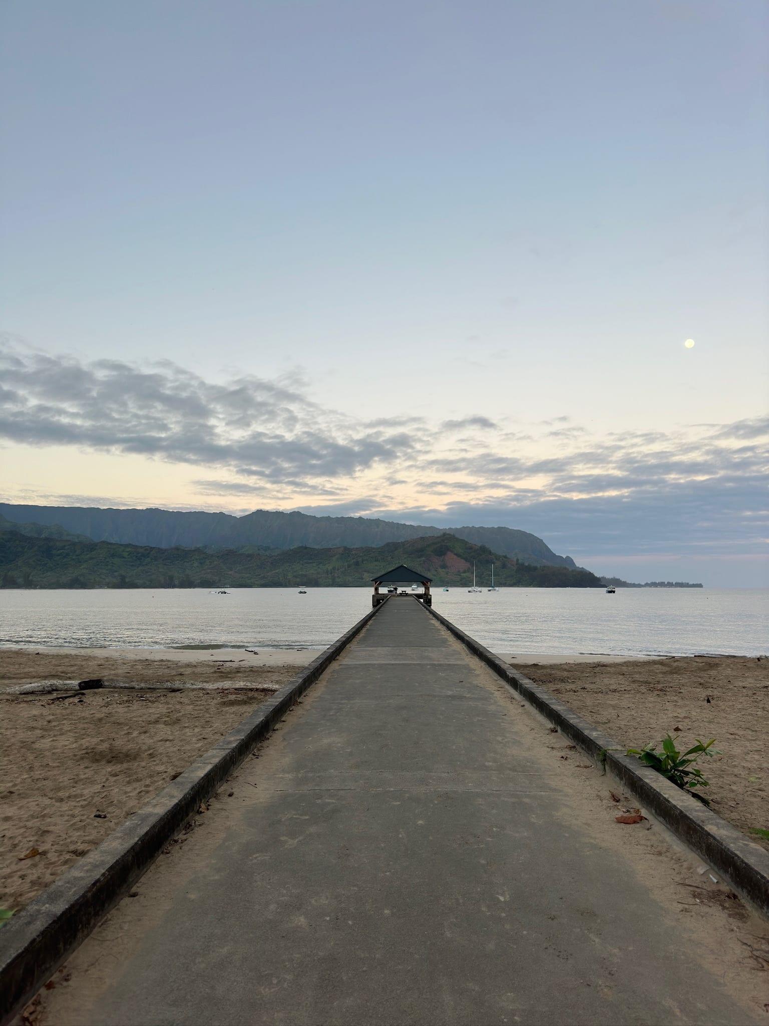Hanalei Pier walkway leading out to Hanalei Bay at dawn with green mountains behind, on Kauai's North Shore near Princeville
