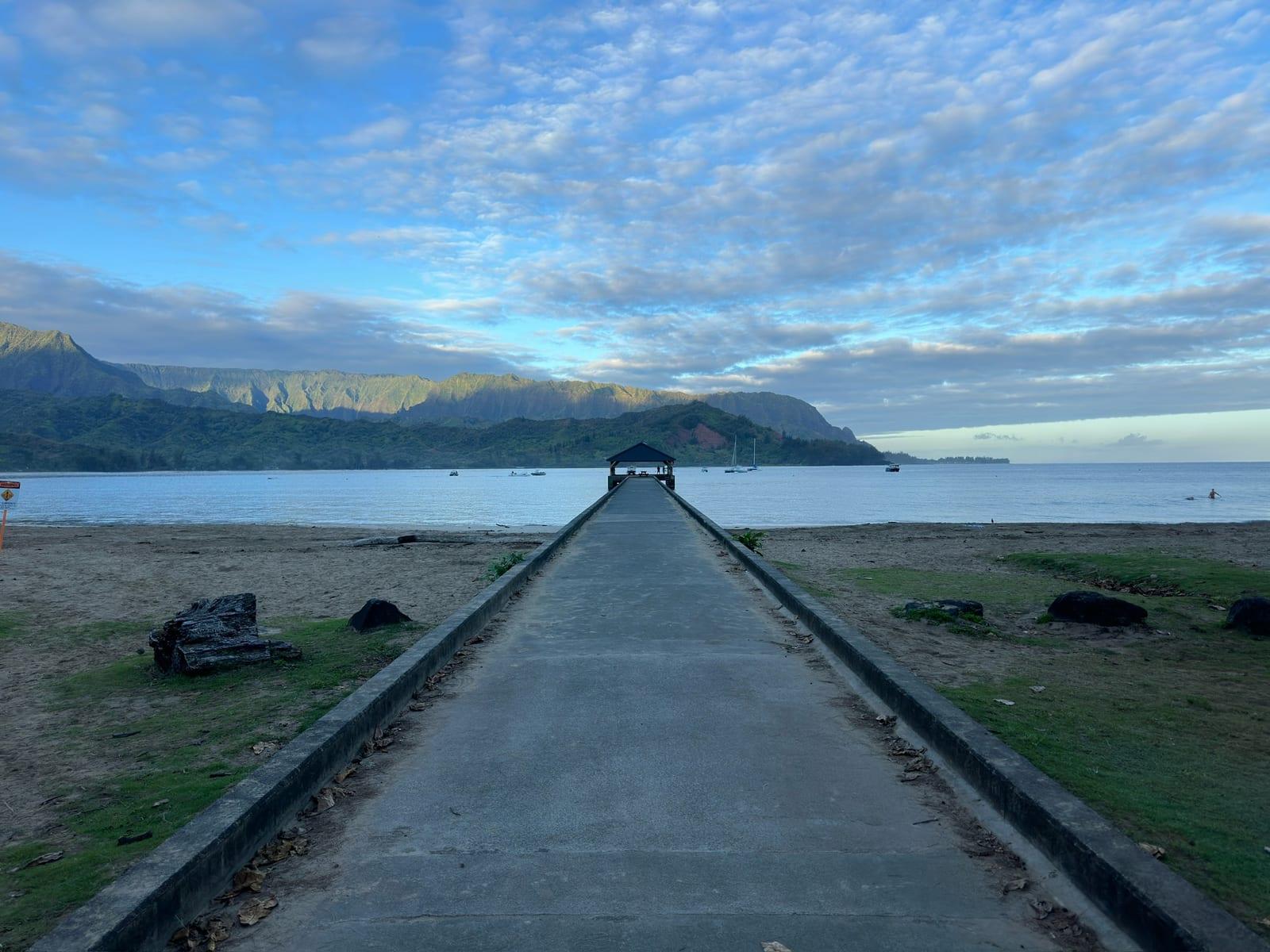 Hanalei Pier walkway leading out over the bay with green North Shore mountains in the backdrop near Princeville, Kauai