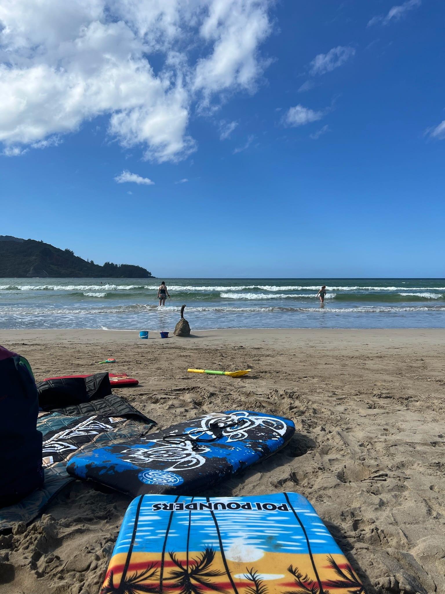 A wide, sunny North Shore beach with boogie boards in the sand, minutes from the Princeville rentals