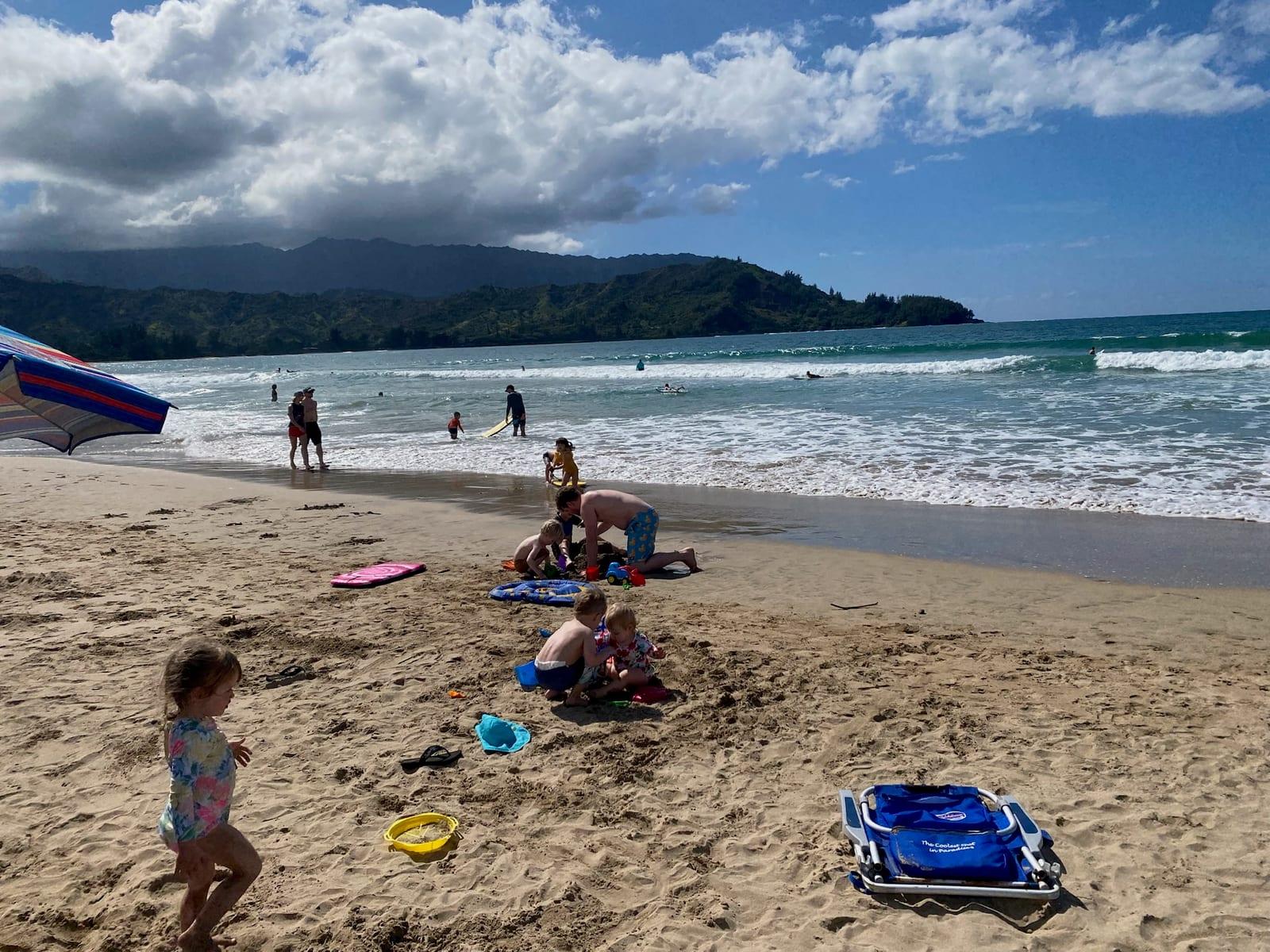 Kids playing in the sand at Hanalei Bay with the North Shore mountains behind them